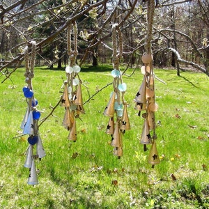 May include: Five wind chimes hanging from a tree branch. Each chime is made of metal bells and glass beads in shades of blue, green, and white. The bells are shaped like cones with a star design.