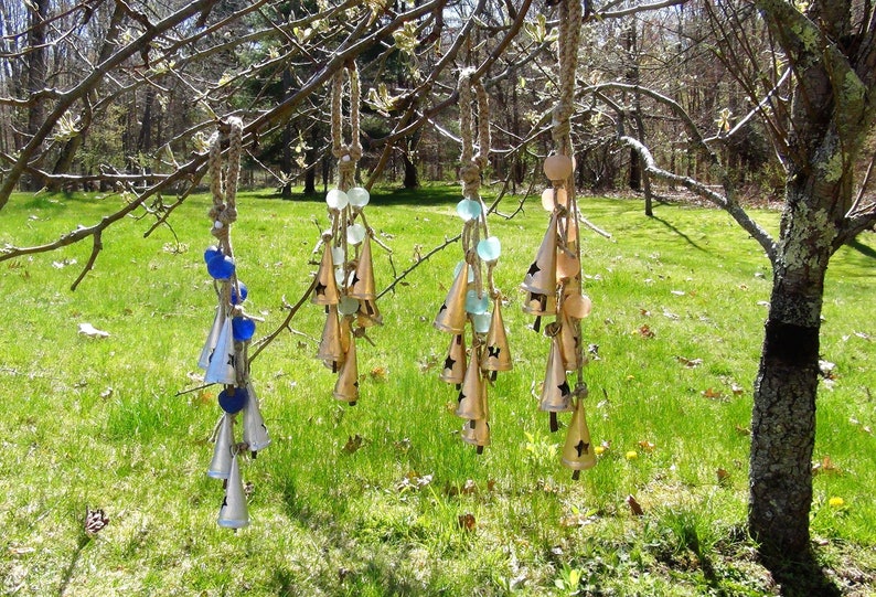May include: Five wind chimes hanging from a tree branch. Each chime is made of metal bells and glass beads in shades of blue, green, and white. The bells are shaped like cones with a star design.
