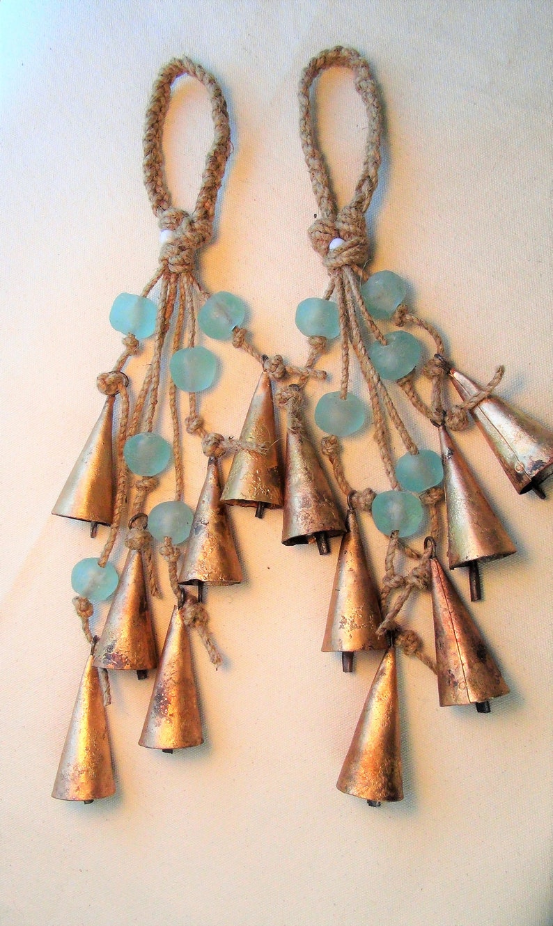 May include: Two sets of brown rope tassels with blue glass beads and copper bells hanging from them.