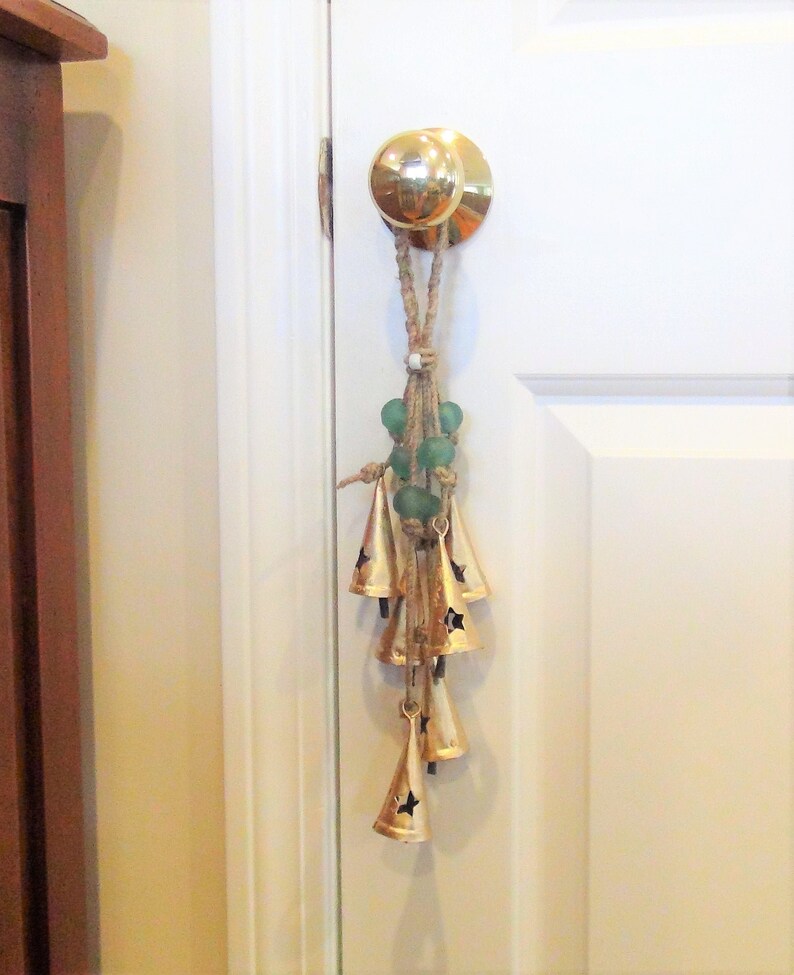 May include: A gold door knocker with a string of green glass beads and a set of gold bells hanging from it.