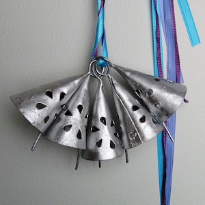 May include: A set of five silver bells with a decorative cut-out design, hanging from a blue and purple ribbon.
