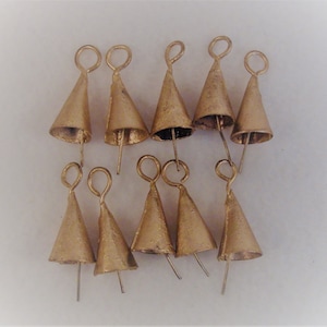 May include: A collection of ten small, gold-colored cone-shaped bells. Each bell has a loop at the top and a metal pin extending from the bottom. The bells are arranged against a white background.