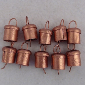 May include: A group of ten small, copper-colored bells with a loop at the top. The bells are arranged in a semi-circle on a white surface.
