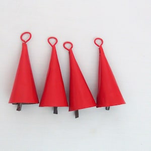 Peut inclure: Quatre clochettes de jingle en métal rouge avec une boucle en haut. Les clochettes sont suspendues à une surface blanche.