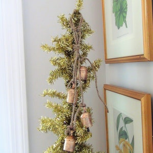 Peut inclure: Un sapin de No&euml;l en paillettes dor&eacute;es d&eacute;cor&eacute; d'une guirlande de petites cloches en cuivre reli&eacute;es par de la ficelle.
