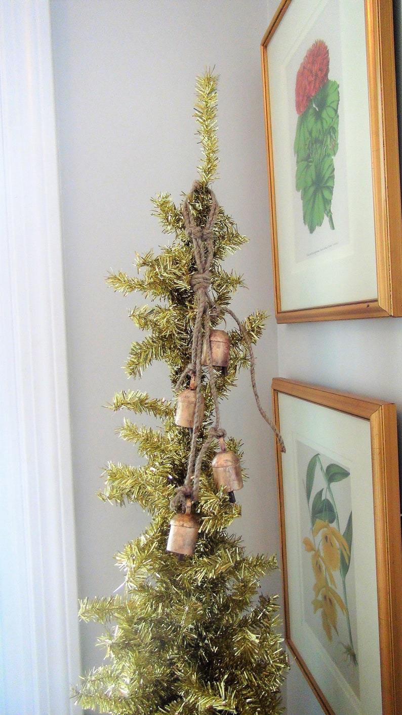Peut inclure: Un sapin de No&euml;l en paillettes dor&eacute;es d&eacute;cor&eacute; d'une guirlande de petites cloches en cuivre reli&eacute;es par de la ficelle.