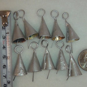 May include: Ten silver jingle bells with a loop at the top and a small wire attached to the bottom. The bells are approximately 1 inch in diameter and are arranged in a cluster on a white surface. A ruler is visible in the background.