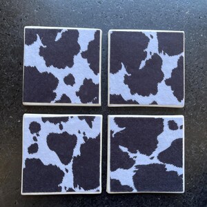 May include: Set of four square coasters with a black and white cow print design.