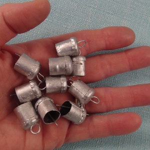 May include: A collection of silver metal bells with a loop at the top. The bells are small and have a smooth, shiny finish.