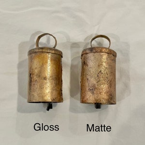 May include: Two antique-style bells, one with a glossy finish and the other with a matte finish. The bells are made of metal and have a rustic look.