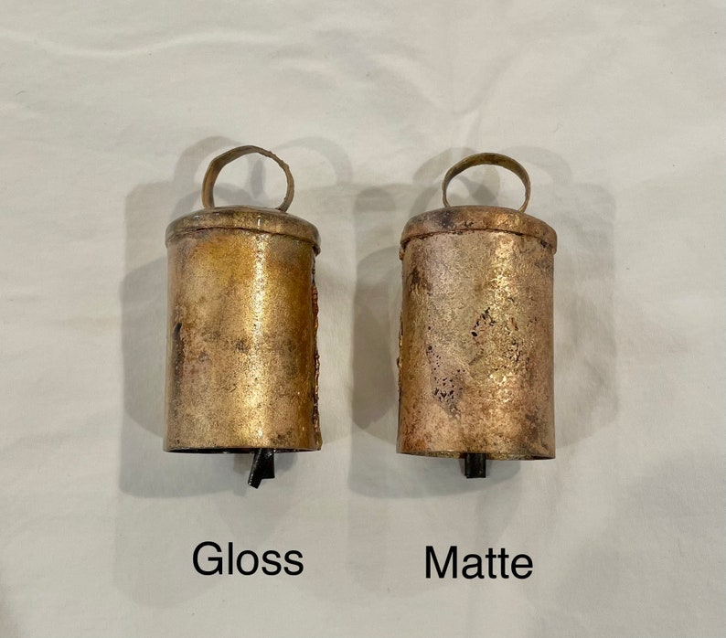 May include: Two antique-style bells, one with a glossy finish and the other with a matte finish. The bells are made of metal and have a rustic look.