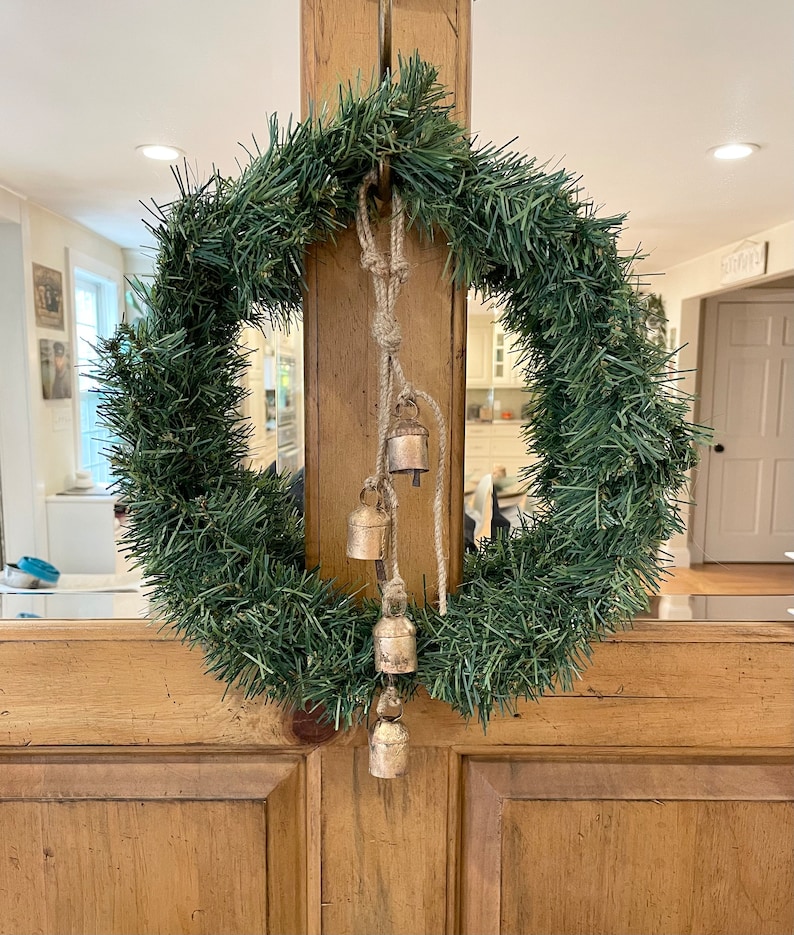 Peut inclure: Une couronne de No&euml;l artificielle verte avec une corde et cinq petites cloches dor&eacute;es qui pendent.