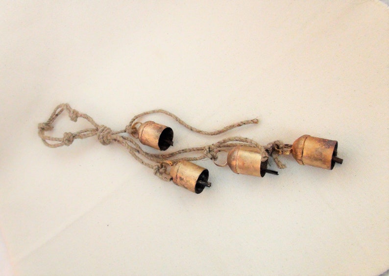 Peut inclure: Un ensemble de quatre petites cloches rustiques suspendues &agrave; une longueur de ficelle naturelle. Les cloches sont en m&eacute;tal et ont un aspect l&eacute;g&egrave;rement vieilli et patin&eacute;.