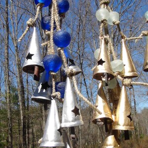 May include: A wind chime with silver and gold bells hanging from a rope with blue and white glass beads. The bells have a star cut-out design.