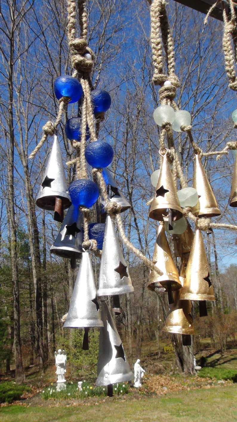 May include: A wind chime with silver and gold bells hanging from a rope with blue and white glass beads. The bells have a star cut-out design.