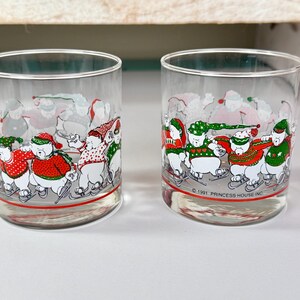 May include: Two clear drinking glasses with a festive winter design. The glasses feature a repeating pattern of polar bears ice skating, wearing red and green sweaters and hats. The base of each glass has a red stripe.