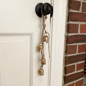 Peut inclure: Une porte avec une poign&eacute;e de porte noire et une cha&icirc;ne de cloches dor&eacute;es qui pendent. Les cloches sont attach&eacute;es ensemble avec de la ficelle et pendent du bouton de porte.