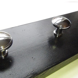 May include: Three silver metal knobs mounted on a black wooden board. The knobs are round and have a shiny finish.