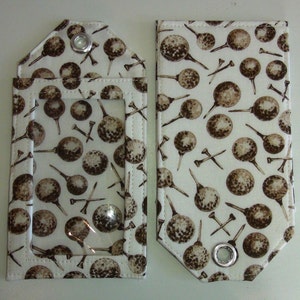 May include: Two white fabric pouches with brown golf ball and tee patterns. The pouch on the left has a clear plastic window. Both pouches have silver eyelets.