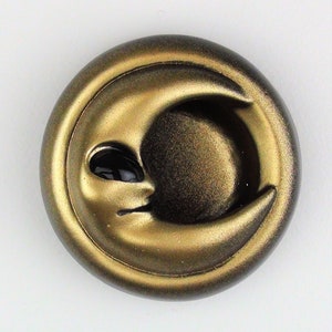 May include: A gold-colored crescent moon with a face, resembling an alien, is the focal point of this decorative button. The button is round and has a raised rim.
