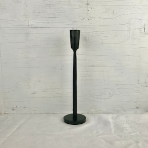 May include: A black metal candle holder with a tall, slender design. The holder has a round base and a simple, elegant silhouette.