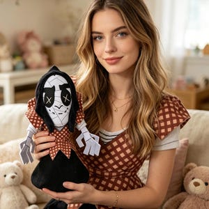May include: A handmade plush doll with a black head covering, white face, and stitched details. The doll has a brown and white checkered bodice and a black skirt. The doll is held in front of a person.