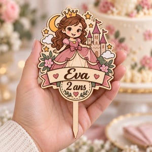 Peut inclure: Un gâteau topper en bois illustrant une princesse aux cheveux bruns avec une couronne et une robe rose, devant un château, une lune et des étoiles. Une bannière affiche le nom Eva et le texte 2 ans, avec des cœurs roses et du feuillage.
