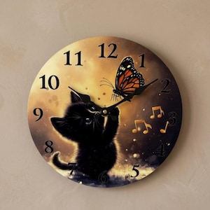 May include: A round wall clock featuring a black kitten reaching toward a monarch butterfly. The background is a gradient of warm gold and dark brown with floating musical notes. The clock face displays black Arabic numerals from 1 to 12.
