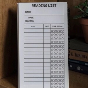 Peut inclure: Un carnet de lecture à spirales blanc avec du texte et des lignes imprimés en noir. L'en-tête indique READING LIST, suivi des champs NAME et DATE STARTED. En dessous se trouvent des colonnes pour TITLE, DATE et un système d'évaluation à cinq étoiles.