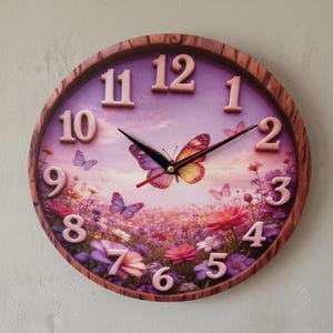 Peut inclure: Une horloge murale ronde avec un cadre imitation bois présentant une scène de prairie avec des fleurs sauvages colorées et des papillons. Le cadran comporte des chiffres en relief de 1 à 12, des aiguilles noires et une trotteuse rouge.