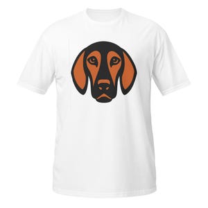 Può includere: T-shirt bianco con un'illustrazione stilizzata della testa di un cane. La testa del cane è nera con orecchie e muso arancioni. La maglietta è realizzata in un materiale morbido e confortevole.