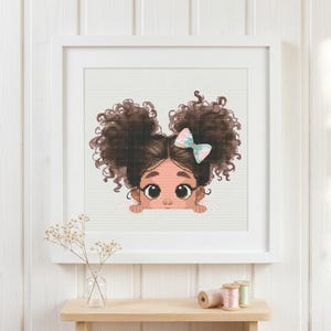 May include: A cross-stitch pattern featuring a cartoon illustration of a child with dark brown curly hair styled in two high puffs. The child has large brown eyes and is wearing a light-colored bow with a subtle pattern, peeking over a ledge.