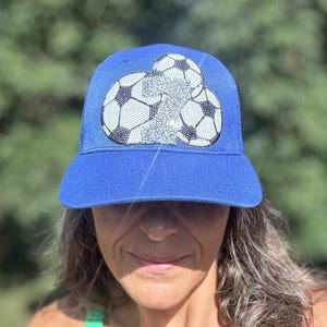 Peut inclure: Une casquette de baseball bleu vif ornée d'un motif central composé de deux ballons de football et d'un grand chiffre sept argenté étincelant. Les ballons présentent un motif classique noir et blanc, tandis que le chiffre sept est recouvert de strass argentés.