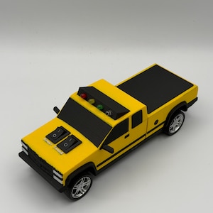 May include: A yellow toy pickup truck with black trim and silver wheels. The hood features two black rocker switches labeled Power and Sound, and the roof has a light bar with red, yellow, and green circular lights. The truck has a black bed cover.