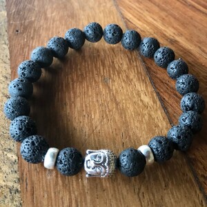 Puede incluir: Pulsera de cuentas de roca volcánica negra con un dije de Buda plateado. La pulsera está hecha de cuentas de roca volcánica natural y presenta un dije de Buda plateado.
