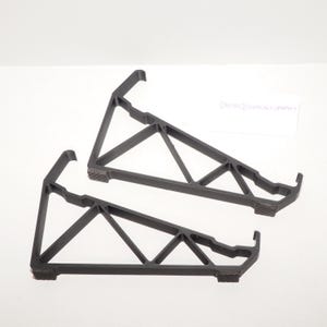 May include: Two black, triangular support brackets. Each bracket has a hook at the top and a textured base. The brackets are designed with a series of angled supports for stability. The Dayton Technology Company logo is visible in the background.