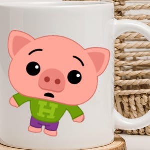 May include: White ceramic mug featuring a cartoon pig character with a pink face, ears, and snout. The pig wears a green shirt with a large "H" and purple pants. The mug has a white handle and is on a wooden coaster.