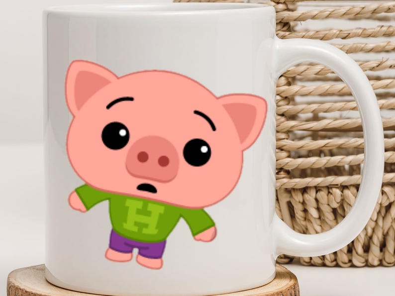 May include: White ceramic mug featuring a cartoon pig character with a pink face, ears, and snout. The pig wears a green shirt with a large "H" and purple pants. The mug has a white handle and is on a wooden coaster.