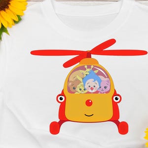 May include: White t-shirt featuring a cartoon helicopter design. The helicopter is yellow and red, with a smiling face and a propeller. Inside the helicopter are several cartoon characters with different colors and expressions.