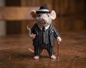 May include: A needle-felted mouse figurine dressed in a black pinstripe suit, white shirt, and black tie. The mouse wears a black fedora with a white band, holds a small cigar with a wisp of smoke, and leans on a thin wooden walking cane.