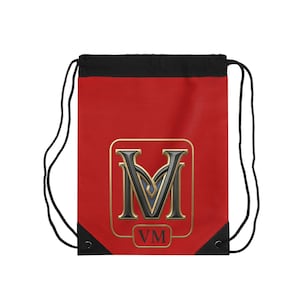 Puede incluir: Mochila roja con cordón y parte superior y cordones negros. La parte delantera presenta un emblema con contorno dorado con una "M" negra y azul y las letras "VM" en un rectángulo con contorno dorado.