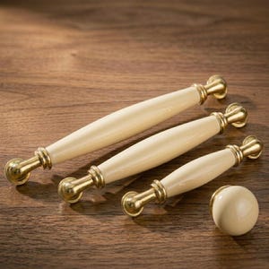 Peut inclure: Tiroirs de meubles crème et un bouton assorti avec une quincaillerie dorée. Les poignées sont de trois tailles différentes, et le bouton est rond. Quincaillerie de conception classique pour les armoires de cuisine ou de salle de bain.