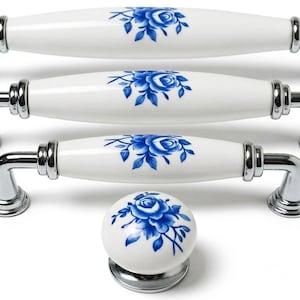 Puede incluir: Tiradores y pomo de armario de cerámica blanca con diseño floral azul. Los tiradores tienen base de metal plateado y forma ovalada. El pomo es redondo con base de metal plateado. El diseño floral presenta una rosa azul y hojas.