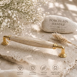 Könnte beinhalten: Porzellangriff in Creme und Gold. Der Griff hat eine Marmoroptik mit goldenen Details und goldfarbenen Metallbeschlägen. Der Text auf dem Stein lautet "PORCELAIN HANDLE, PREMIUM QUALITY, TIMELESS DESIGN."