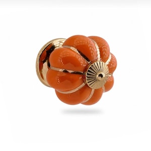 May include: Orange and gold cabinet knob with a pumpkin-like design. The knob features a glossy orange finish with gold accents and a gold base. This decorative hardware is suitable for drawers, cabinets, and furniture.