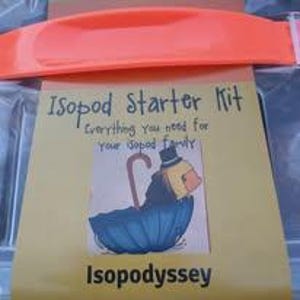 May include: A yellow card with the text "Isopod Starter Kit" and "Everything you need for your isopod family." An illustration of a duck-like creature with an umbrella is also on the card. The card is inside a clear container with an orange handle.