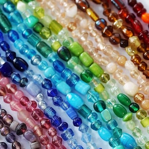May include: A close-up of colourful beaded strands in a rainbow of hues. The beads vary in shape and size, with colours ranging from deep blues and greens to warm oranges and reds. The beads are strung together, creating a vibrant display.
