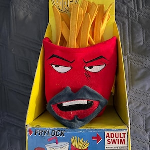 May include: A plush toy of Frylock from Aqua Teen Hunger Force, featuring a red face with a dark blue mouth and yellow fries. The toy is in a yellow box with the show's logo and "Adult Swim" branding.