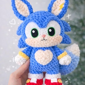May include: A handmade blue and white crochet plush toy resembling a cartoon character with large green eyes, a heart-shaped chest, and red shoes. The toy has a lightning bolt on one ear and a white tail. The plush is approximately 8 inches tall.