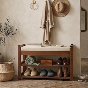 Peut inclure: Un banc &agrave; chaussures rectangulaire en bois dot&eacute; d'un coussin d'assise beige et de deux &eacute;tag&egrave;res de rangement ouvertes. Les &eacute;tag&egrave;res contiennent une couverture verte roul&eacute;e, une bo&icirc;te en bois et plusieurs paires de chaussures.